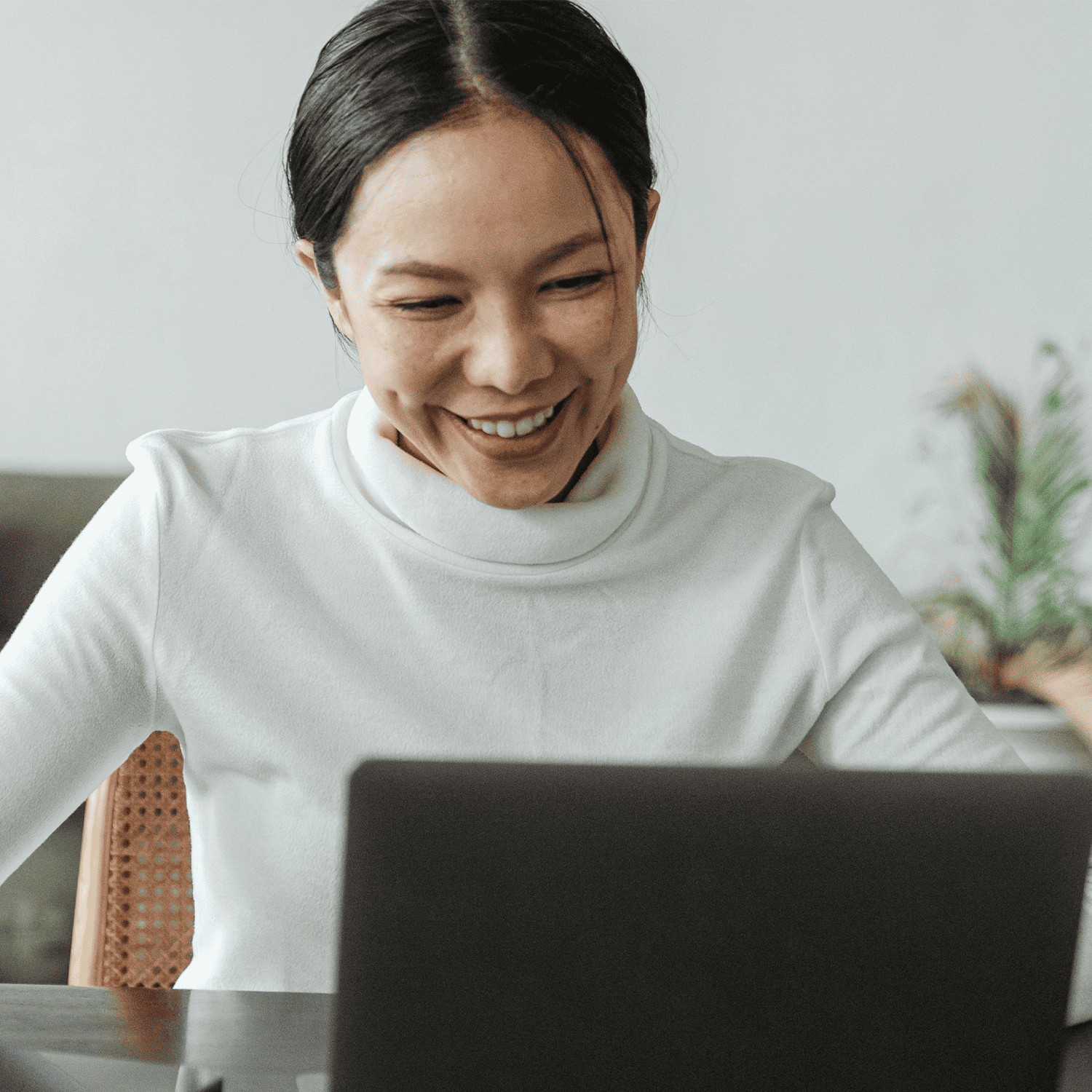 Person wearing a white turtleneck smiling in front of a laptop.