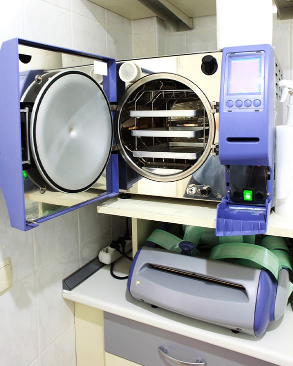 Person wearing gloves handling surgical instruments in a sterilization chamber.