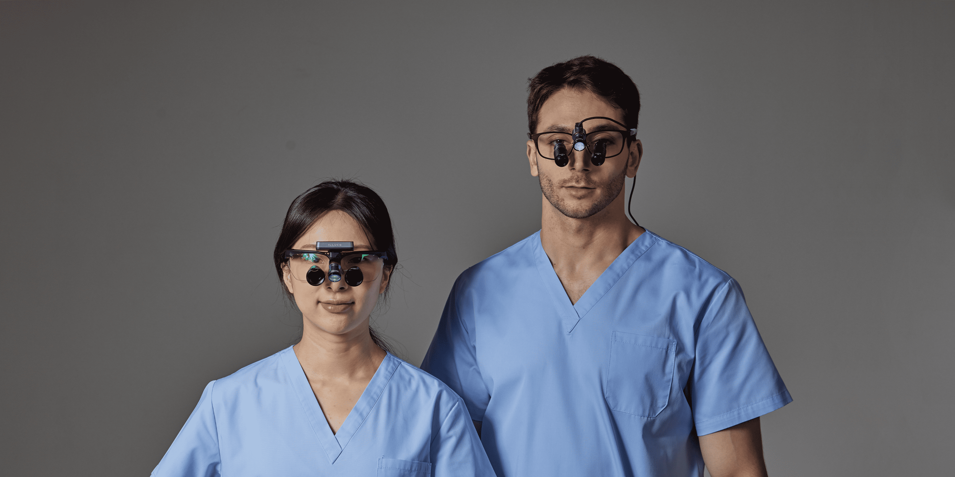 Two individuals in blue scrubs with ILLUCO Loupes