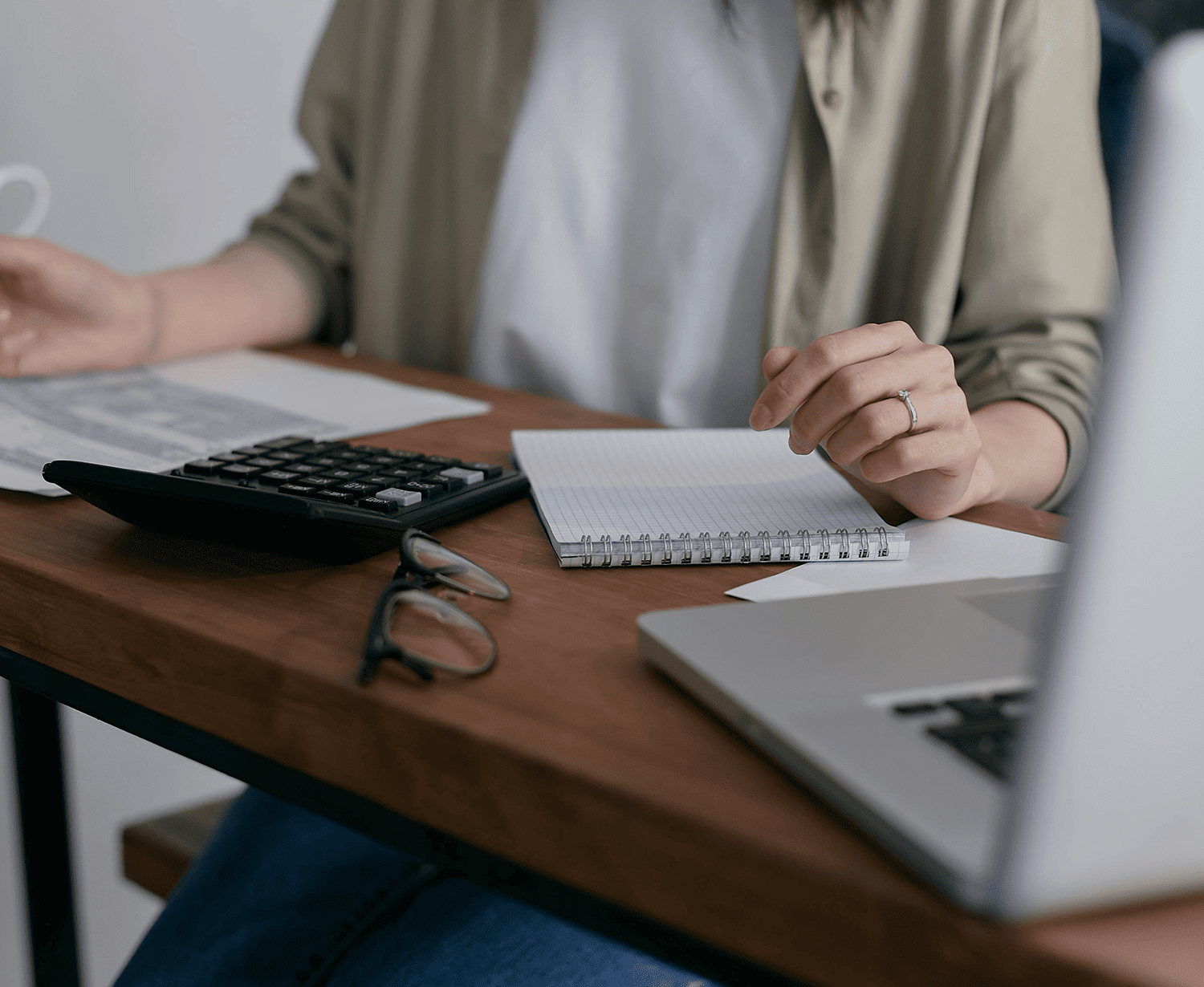 Person working at a desk with a laptop, notebook, and calculator.